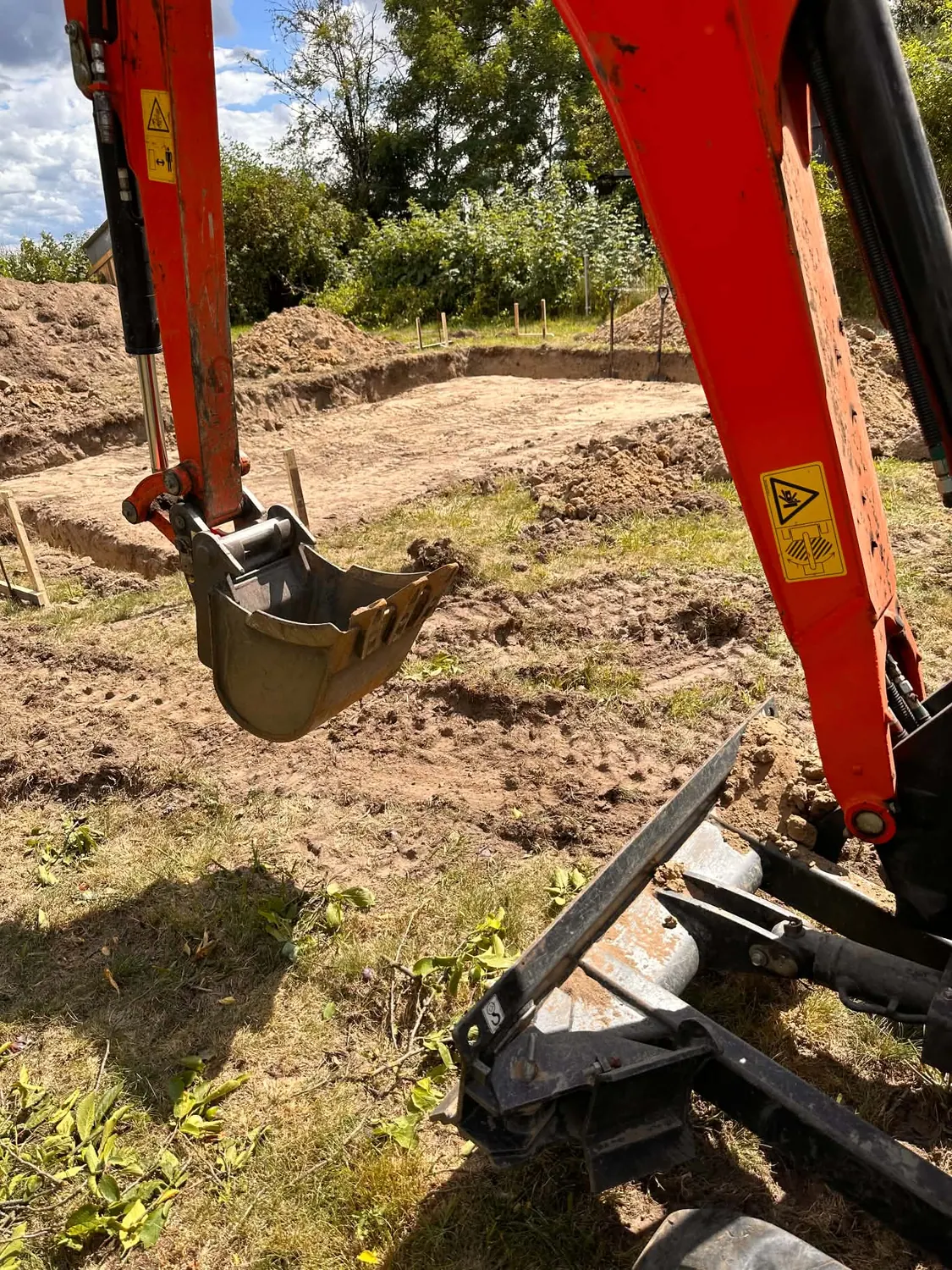 Wykop pod fundament wykonany minikoparką na działce, widok na ramię i łyżkę maszyny.