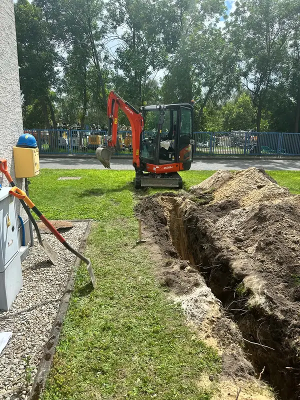 Wykop prowadzony wzdłuż budynku obok skrzynki elektrycznej, minikoparka przy hałdzie urobku.
